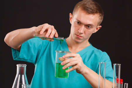 A man scientist pours liquid from a test-tube into another utensil in a robotic table on a black backgroundの写真素材
