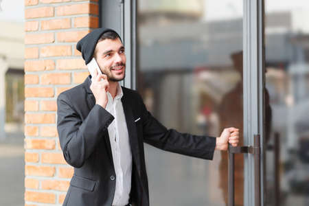 Young businessman speaks on the phone and opens the door of the building