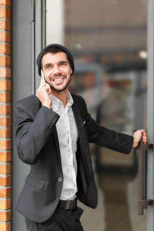Young businessman speaks on the phone and opens the building door looks asideの写真素材