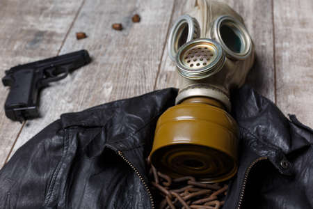 On the floor is a leather jacket on which lies a gas mask and a chain, next to it is a pistol.の写真素材
