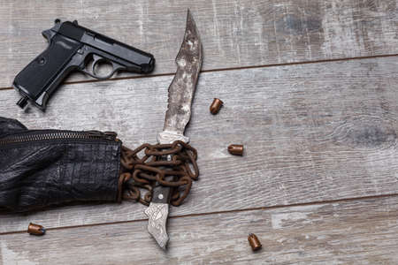 A leather jacket from the sleeve, an old chain is visible, in which there is an rusty knife, next there is a pistol.の写真素材