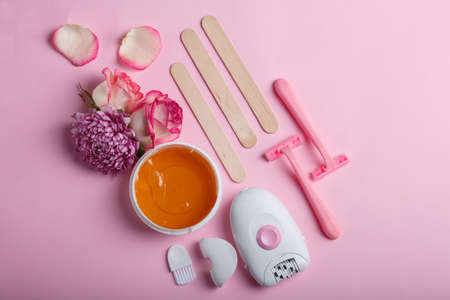Electric epilator, razor, wax and spatula. There are several buds of flowers. View from above.の写真素材