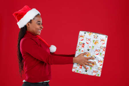 African-American girl holds a gift box on her outstretched hands and laughs . On a red background.の写真素材