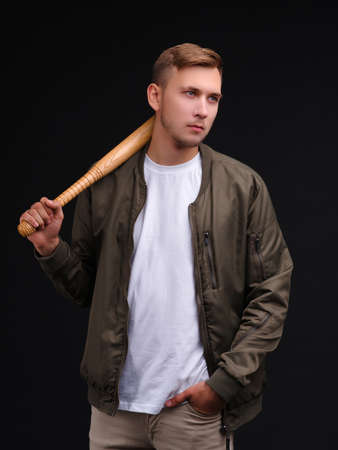 A guy in a jacket, stands and holds a bat on his shoulder. On a black background.の写真素材