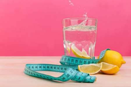 A glass of water with a slice of lemon, next to a whole and a few quarters of lemon and tape a centimeter.の写真素材