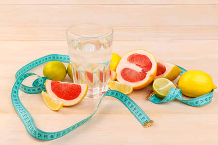 On the table sliced lemon, grapefruit and lime near a glass with clean water and tape centimeter. Indoors.の写真素材