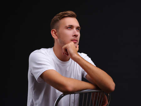 A guy, sitting on a chair and staring into the distance with a serious pensive look.の写真素材