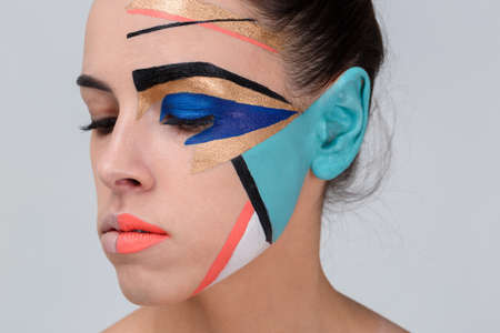 An attractive girl, with a colorful creative geometric greasepaint on her face looks down.