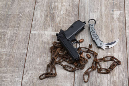 The layout of a black pistol, several scattered cartridges, a folding knife and an old rusty chain.