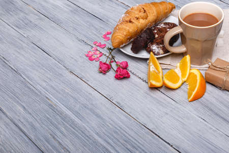 With the right croissant with a chocolate cake and an orange on a gray wooden background, next are...