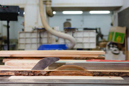 The machine saws the board close-up on a blurred background. Side view