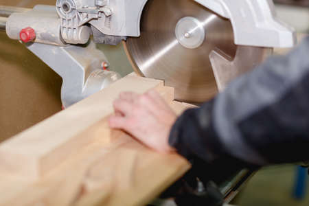 Hands of the worker saw a bar on a circular saw in focus close-up