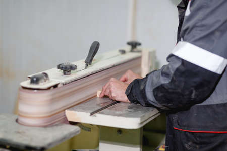 The worker in the form grinds the part on the grinding machine close-up. Side view at an angle
