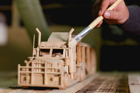 Hands of the worker in the form of paint the exhaust pipes of a wooden truck on a blurred...