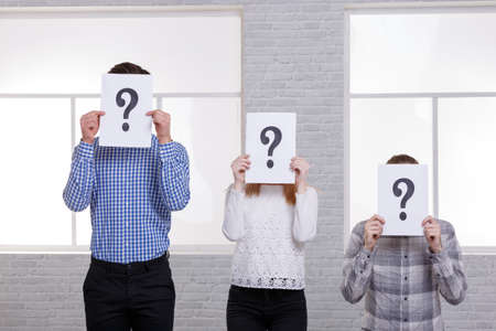 Guys and a girl close their faces with signs with questions. The girl in the middle. Lined up in the...