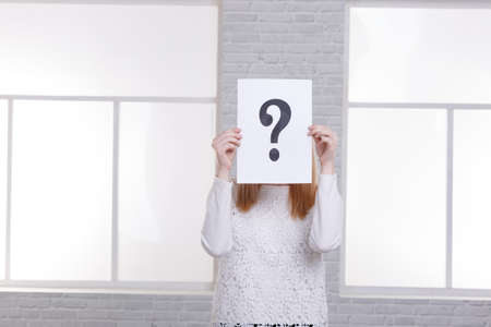 A young girl in a white sweater covers a sheet with a question mark