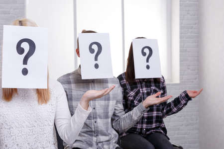 Three people with closed faces with sheets with a question mark are sitting next to a ladder with...