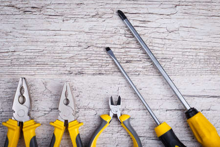Pliers yellow with black and nippers, two screwdrivers lie below are shown not completely on a gray...
