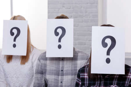 Three people with closed faces with sheets with a question mark