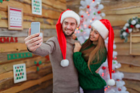 The guy hugs the girl and makes selfie on the background of the dressed up treeの写真素材