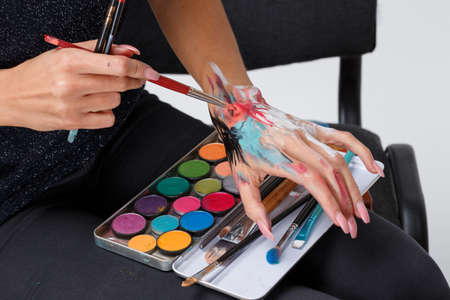A close-up smeared hand make-up artist in paint, holds a brush, and a color palette of paints, selects the color of the paint by doing strokes on the hand.の写真素材