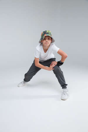 The boy stretches his leg muscles and leans on the thigh against a gray background