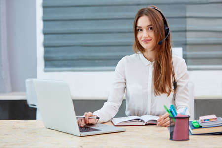 Girl operator working behind a laptop on the desktop looking straightの写真素材