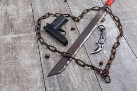 Rusty chain in the shape of heart and machete on a wooden background. Top view from an angle