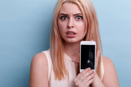 A girl in shock shows a close-up of a broken phone on a blue background