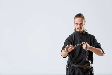 A ninja man pulls a chain between his fists against a gray background