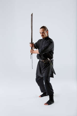 A ninja man concentrates his sword with both hands in front of him against a gray backgroundの写真素材