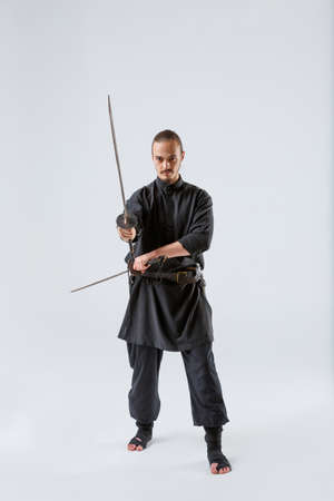 A ninja man holds perpendicular swords in his hands against a gray backgroundの写真素材