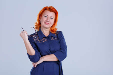 A woman is thoughtfully holding glasses in her hand on a gray backgroundの写真素材