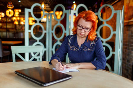 A woman sits at a table in a cafe and makes notes in a notebookの写真素材