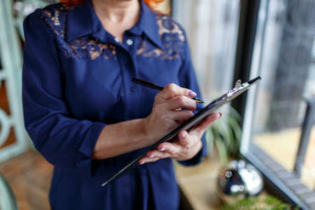 A woman is making notes in a tablet in her hand on a blurred backgroundの写真素材