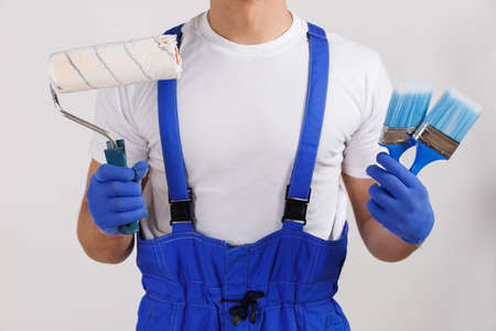 A worker holds a roller and paint brushes close-up on a white backgroundの写真素材