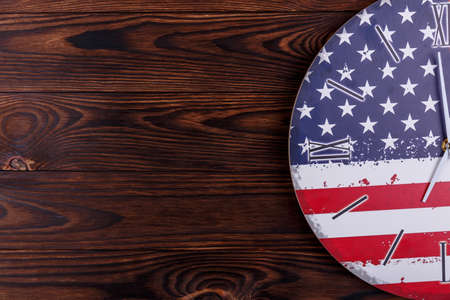 A clock in the coloring of the American flag is shown in large on a half on a wooden backgroundの写真素材