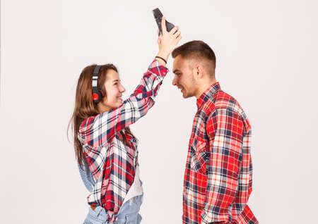 A girl in headphones takes headphones off a guy on a gray background