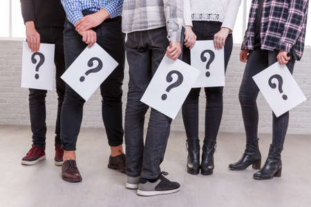 A group of people are shown incompletely with their hands down in which the sheets with the question markの写真素材