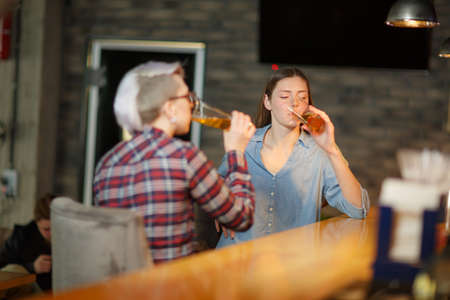 Two girls in a bar drinking beer. Indoors in a public place.の写真素材