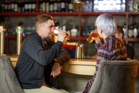 A guy with a beard and a girl with short blond hair, sitting in a bar and drinking beer. Indoorsの写真素材