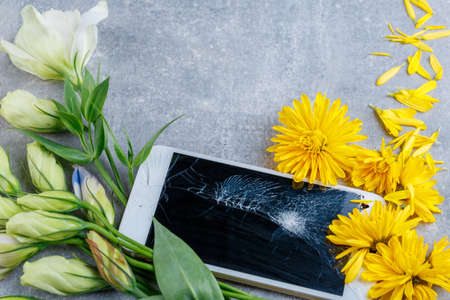 A broken touch and stylish phone lies horizontally near by flowers yellow and white close-up on a...