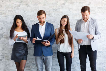 A group of boys and girls is busy, using a smartphone, a tablet and looking at documents.の写真素材
