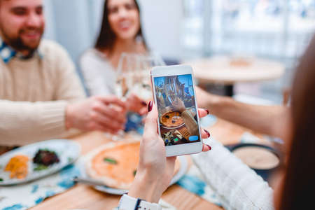 Female hand making photo of group of people having supper in cafe.の写真素材