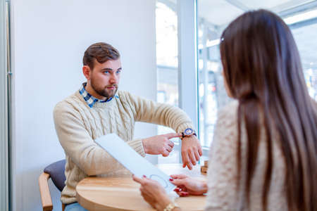 A couple on a date in a cafe, the guy points at the clock, indignant that the girl was late.の写真素材