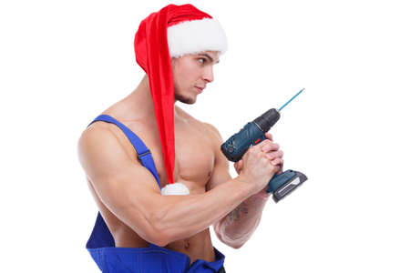A serious guy, in a uniform and a Santa hat, stands sideways and holds a drill in his hand. Isolated on white.の写真素材