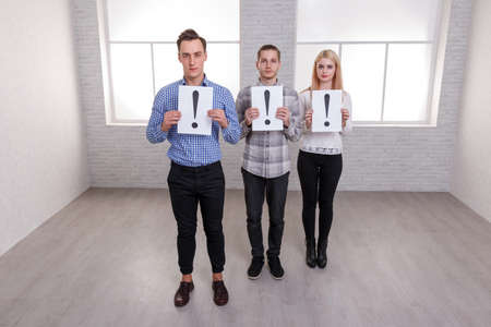 Two guys and a girl stand and hold paper sheets with a exclamation point.の写真素材