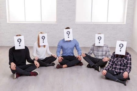 A group of people are sitting on the floor, on their faces are paper sheets with a question mark,.の写真素材
