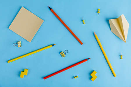 On a blue background are multi-colored pencils, clips, paper stickers and a paper airplane. View over.の写真素材