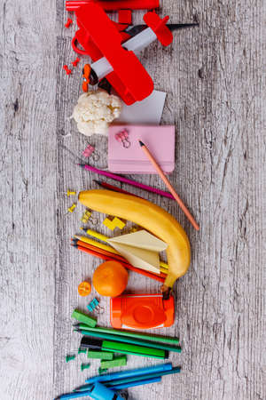 On a table layout in a row is a chancellery, a red toy airplane and a piece of cauliflower and a banana.の写真素材